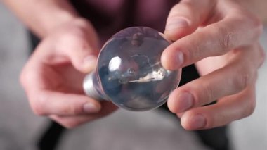 Ellerin dikkatlice parlak bir ampulü döndürme perspektifi cam dokusu, iç lif ve metal vida üzerinde odaklanarak bulanık bir arka plan karşı.