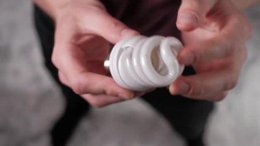 Erkek eller dikkatle tutun ve inceleyin beyaz spiral floresan lamba CFL, bükülmüş tüp tasarımı gösterir ve enerji tasarrufu ampul teknolojisinin tabanını vidalama.