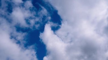 Dalgalanan beyaz ve gri bulutların zaman çizelgesi parlak mavi gökyüzünde hareket ederken, gün ışığında oluşumlar olarak ortaya çıkan açık yamalar.