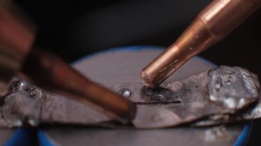 Benek kaynaklama elektrotlarının aşırı yavaş çekimde batarya terminaline metal bir sekme ile birleşmesi ve endüstriyel bir ortamda sönük dumanın ortaya çıkması..
