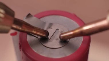 Pembe şarj edilebilir batarya hücresinin en üst ucuna metal plaka takan kaynak elektrotları gösteren aşırı yakın çekim. Enerji depolama aygıtları için hassas imalat.