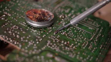 Erimiş lehim lehimini yeşil bir PCB 'nin elektronik bileşenlerine reçine akışı kullanarak uygulayan kızgın demir uçlarının makro görüntüsü. Onarım işlemi sırasında ısıtmalı bağlantıdan duman yükselir.