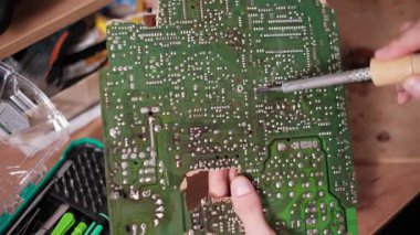 Teknisyenlerin ellerinin yakın plan görüntüsü lehim kullanarak karmaşık yeşil baskılı devre kartının tamiri ve tezgahın kırılan kısmının onarılması için kullanılıyor.
