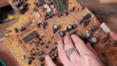 Bir atölye ortamında elektronik tamiri sırasında kompleks baskılı devre kartından lehimleme demiri kullanarak ve kapasitör bileşenini çıkarmak için ellerin yakın plan görüntüsü...