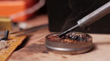 Sıcak lehim ucunun tüten bir reçine akışının teneke kutusuna batırıldığı aşırı yavaş çekim videosu, çalışma tezgahındaki elektronik bileşen lehimlemesi için aracı hazırlıyor.