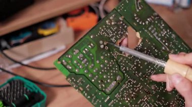 PCB montaj sırasında veya tamir sırasında yeşil baskılı devre kartının arka tarafındaki lehim eklemlerini dikkatlice eritmek için lehim aleti kullanan bir elektronik teknisyenin ayrıntılı görüntüsü..