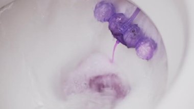 Beyaz seramik tuvalet sifonunun Macro 4K videosu, canlı köpük salgılayan mor top spreyini aktifleştiriyor, tuvaletin temizliğini ve temizliğini gösteriyor..
