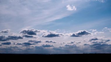 Dinamik zaman dilimi, mavi gökyüzünde hızla hareket eden kümülüs bulutlarını yakalar. Karanlık bir ufkun üzerinde kısa bir süre parlayan güneş halesi ile birlikte..
