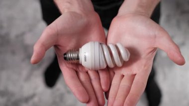 Üst görüntüde erkek eller beyaz spiral florasan lamba tutuyor. Enerji verimliliği, ışıklandırma teknolojisi ve güç korunumu kavramı. Statik çekim, sabit görüş.