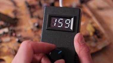 Elektronik voltaj kontrolörünün düğmesini çeviren bir elin yakın çekimi. Dijital ekran, ekipman için güç veya voltaj ayarlarını belirten dalgalanan sayısal değerleri gösterir.