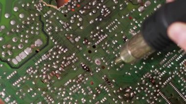 Teknisyen olarak yakınlaştırma görüntüsü, bir atölyede elektronik tamir veya montaj sırasında yeşil baskılı devre kartındaki lehim eklemlerini ısıtmak için sıcak hava yenileme istasyonu kullanır...