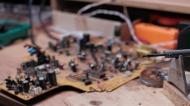 Metal tezgahının üzerinde duran kızgın bir lehim demirinin yakın plan fotoğrafı, duman yayıyor. Arka plandaki ahşap tezgahta bulanık bir devre kartı ve aletler görülüyor..