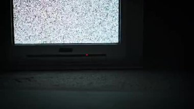 Karanlık bir ortamda titreşen statik gürültüyü gösteren eski bir CRT televizyonunun yakın çekim görüntüsü. Kumlu siyah beyaz ekran dokusuna ve kırmızı güç ışığına odaklan. Kayıp sinyal konsepti.