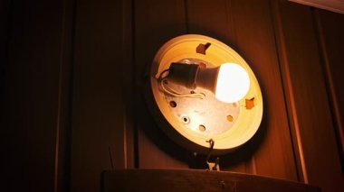 Duvardaki lamba tabanındaki ışığın düşük açılı görüntüsü soketi ve karanlık panelli bir duvara bağlı kabloları ortaya çıkarıyor. Çekim içerideki işleyişi açıkça gösteriyor.