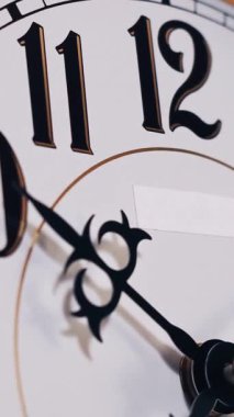 Dikey zaman çizelgesi, klasik analog saat yüzünün yakın çekimini gösteriyor. Süslü elleri beyaz kadranın üzerinde hızla dönüyor. Hızlı zaman geçişini gösteriyor..