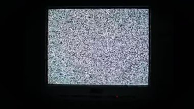 Karanlıkta titreşen analog beyaz gürültüyü gösteren retro televizyonun orta boy görüntüsü. Klasik CRT ekranı, eski teknoloji ve yayın sorunlarını vurgulayarak hiçbir sinyal karışıklığı göstermiyor.