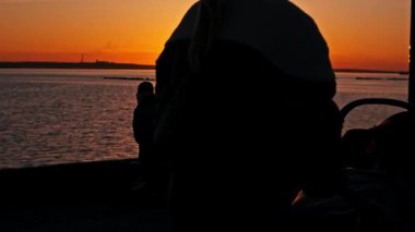 Suda dinlenen insanların siluetleri, turuncu bir gün batımını seyreden bir kadın, bir bankta yürürken ve sakin bir göl ya da deniz manzarasının keyfini çıkarırken.