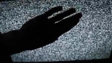 Bir elin silueti uzanır ve titreyen statik gürültüyü gösteren bir televizyon ekranına dokunur. Medyayla etkileşim, paranormal aktivite, korku veya teknolojinin içinde sıkışıp kalma kavramı.