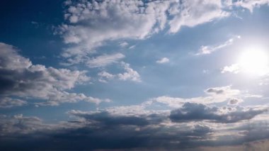 Mavi gökyüzünde hareket eden kara bulutların zamanı, parlak güneş ışınlarının delip geçmesi, siluetli bir manzaranın üzerindeki sahneyi aydınlatıyor. Zaman içinde atmosferik hava dinamikleri.