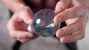 Ellerin dikkatlice parlak bir ampulü döndürme perspektifi cam dokusu, iç lif ve metal vida üzerinde odaklanarak bulanık bir arka plan karşı.