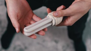 Erkek ellerinin daha eski bir U şeklindeki floresan ampulü dikkatlice incelerken yakın plan görüntüsü. Cam tüpleri ve tabanı incelemeye odaklan. Enerji tasarrufu kavramı ve ışıklandırma seçimi.
