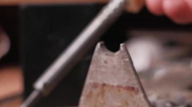 Metal bir standın üzerinde duran kızgın bir lehim ucunun makro yakın çekimi, duman yayıyor. Erimiş lehim, bir el kısaca çıkarmadan ve aracı değiştirmeden önce ucunda parlar.
