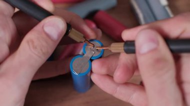 Ellerin makro görünümü, kaynak nikel şeridini iki mavi 18650 lityum-iyon batarya, enerji bağlantısı ve DIY yöntemleri ile yeniden şarj edilebilir bir paket inşa etmek için anahtar bir adım gösterir