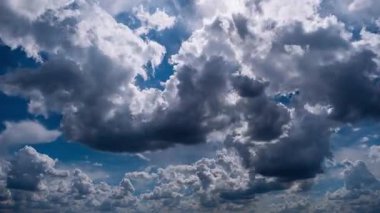 Zaman çizelgesi beyaz ve gri kümülüs bulutlarının parlak mavi bir gökyüzünde hızla sürüklendiğini gösteriyor. Güneş dinamik bulut oluşumlarını vurgular, hızlı hareket ve değişen hava hissi yaratır..