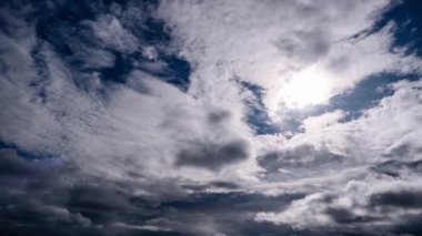 Zaman çizelgesi, derin mavi gökyüzünde hareket eden dramatik kara bulutları, parlak güneşin çarpıcı bir kontrastı oluşturduğunu gösteriyor. Değişen bulut katmanları, karamsar ve güçlü bir bakış açısı sunar..