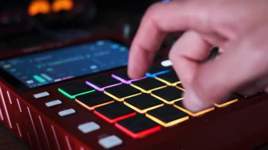 Müzisyenlerin yakın çekimleri modern bir ritim yapıcının renkli ve aydınlatıcı pedlerine dokunuyor. Profesyonel ses ekipmanları karanlık bir stüdyoda müzik prodüksiyonunda parlıyor..