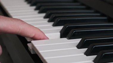 Bir bestecinin dijital klavyenin beyaz tuşlarına tek bir nota basarken yakın plan görüntüsü. Çekim müzik yaratma, ölçek uygulama veya müzikal eğitim sürecini vurguluyor.