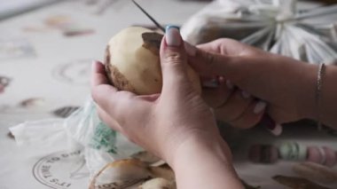 Bir kadın elleri plastik bir torba üzerinde çiğ bir patatesi ustalıkla soyar ve keskin bir bıçakla kirli derisini yüzer. Bu yakın plan ev yapımı yemek hazırlama sürecini vurguluyor..