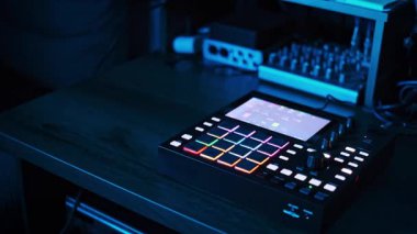 Renkli, titreşimli RGB ışıkları ve düğmeleri olan Beatmaker ahşap bir stüdyo masasında oturuyor. Stüdyonun çevre ışıklandırması renk değiştirir ve dinamik atmosfer müzik üretimine katkı sağlar..
