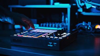Modern bir stüdyoda kırmızı bir beatmaker üzerinde çalışan bir müzisyenin orta ölçekli resmi, müzik prodüksiyon sürecini dinamik ışıklandırmayla gösteriyor..