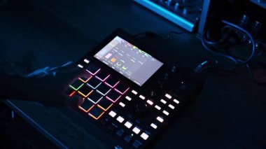 Tek bir parmak, canlı kırmızı bir dijital müzik örnekleyicisi üzerinde parlak pedlere basar. Bu da stüdyoda yaratılış sürecindeki kesin kontrol ve etkileşimi gösterir..