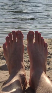 Göl ya da denizin kenarındaki sıcak kumda uzanan çıplak ayaklı bir adamın ilk insan görüntüsü. Nazik su dalgaları, güneşli ve sakin bir günde arka planda parıldarken ayak parmakları hafifçe kıpırdar..