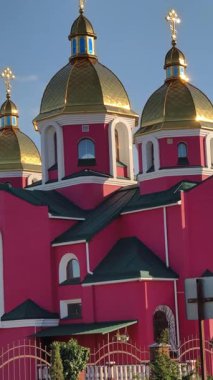 Pembe bir Ortodoks kilisesinde, mimari detaylarını, altın kubbelerini ve güzel mavi bir gökyüzüne karşı çaprazlamasını gösteren dikey format videosu. Huzurlu ruhsal bir sahne.