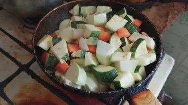 Kabak ve havuç da dahil olmak üzere taze kesilmiş sebzelerin yakın plan görüntüsü, eski bir kızartma tavasında pişiyor. Malzemeler, ev yapımı pişirme işlemi sırasında çok eski, kırsal bir gaz ocağında kaynıyor..