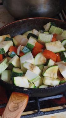 Kabak, havuç ve soğan da dahil olmak üzere doğranmış sebzelerin, sıcak, siyah bir tavada kaynatılıp pişirildiği yakın plan dikey çekimi. Evde sağlıklı bir vejetaryen yemeği pişirme süreci..