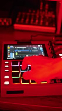 Dikey bir video kırmızı bir MIDI davul makinesinde parlayan pedleri yakalar ve dinamik olarak değişen pembe, mavi ve kırmızı ışıklar altında modern elektronik ritimler yaratır..