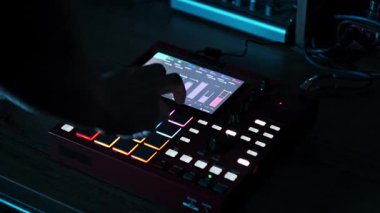 Bir müzik yapımcısının elleri, çok renkli aydınlatma yastıkları ve loş ışıklandırılmış stüdyo ortamında bir grafik ekranı olan kırmızı dijital bir beatmaker numunesi çalarken görülüyor..