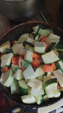 Dikey yakın çekim taze, doğranmış kabak ve fırında kızartılmış tavada kaynayan havuçları gösteriyor. Sağlıklı, basit, ev yapımı vejetaryen yemeğinden buhar yavaşça yükselir..