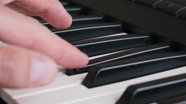 Bir müzisyenin eli klavyede hareket eder ve bir sentezleyicinin siyah ve beyaz tuşlarında melodi çalar. Bu yakın çekim çalışması bir piyanistin sanatsal sürecine odaklanır..