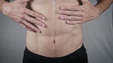 Karın kaslarını ovuşturan, rahatsızlığını, hazımsızlığını veya karın ağrısını ifade eden tişörtsüz bir adamın yakın çekimi. Elleri karın bölgesine baskı yapıyor, bu da bir sağlık sorunu ya da kramp olduğunu gösteriyor..