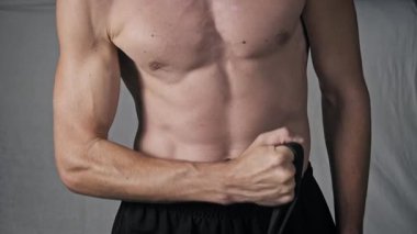 Gövdesi belli bir sporcunun, siyah direniş bandı kullanarak pazularını kıvırırken, bir stüdyo ortamında kas egzersizi yaparken yakın plan çekimleri..