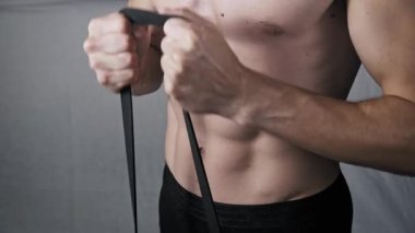 Formda bir adamın kaslı gövdesine yakın çekim. Göğüs ve kol egzersizi yaparken, iki eliyle bir siyah direnç bandını gererek kas tanımı oluşturur..