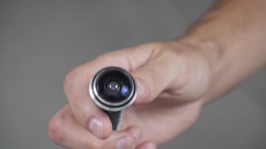 Makro görüntüde küçük bir kamera tutan bir el görülüyor. Konumuz, modern ev güvenliği ve gözetleme ekipmanlarının optik detaylarını vurgulayan balık gözlü mercek..
