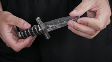 Klasik çelik bir hançerin keskin kenarını ve kabzasını dikkatlice inceleyen birinin yakın çekimi. Bu tarihi silah tehlikeyi, ustalığı ve ortaçağ savaşını temsil ediyor..