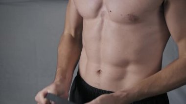 Gömleksiz bir sporcunun gövdesine yakın çekim. Dönüşümlü güç egzersizi yapıyor. Siyah elastik bir bandı iki eliyle bükerek karın ve kol kaslarını çalıştırıyor..