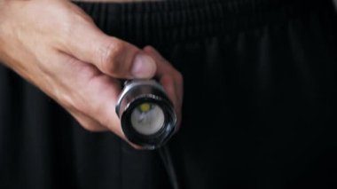 Siyah pantolondan el fenerini alan ve güçlü parlak ışığını doğrudan kamera lensine doğrultan bir elin yakın çekimi dramatik bir mavi ışık efekti yaratır..
